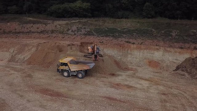 Drone aerial shot of dump truck being loaded by excavator with sand and gravel at quarry