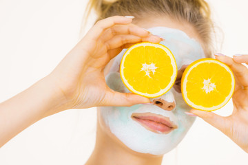 Girl mud mask on face holds orange fruit