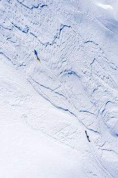 Drone image of three people ski-touring in high mountains in winter. Minimal style image with snow texture and shadows. 