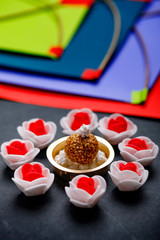 Til Gul OR Sweet Sesame Laddu with Miniature Fikri and Kite model with haldi Kumkum and sugar crystals for Makar Sankranti festival over moody background, selective focus