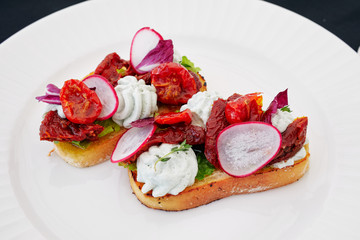 two sandwiches with vegetables lie on a white plate, with radish, tomato, pepper, garlic, herbs and white bread