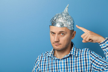 Man with a serious face shows a finger at a cap with aluminum foil. Protects from reading think