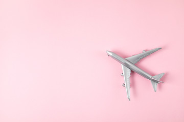 Miniature silver airplane over pink background. Travel tourism, airlines, low cost flights concept. Top view, flat lay.