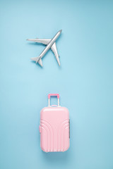 Obraz premium Miniature airplane and suitcase over blue background. Travel preparation, tourism, airlines, low cost flights, baggage packing concept. Top view, flat lay.