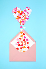 Pink envelope with heart shaped confetti over the blue background. Love, letter, message, saint valentines day concept. Flat lay, top view