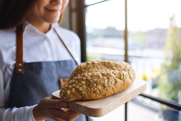 A waitress holding and serving a loaf of whole grain bread