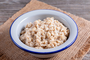 Delicious oatmeal porridge with raisins, butter and honey on a white plate on a wooden background