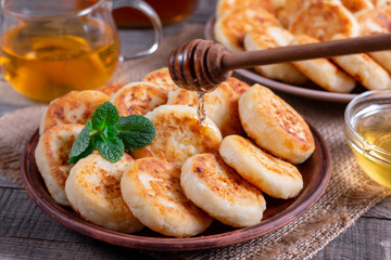 Cottage cheese pancakes, syrniki with honey on a plate on wooden background