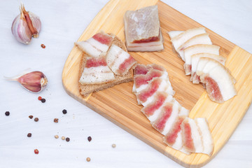 Raw bacon or ukrainian salo on wooden board with garlic, pepper on white background. Top view, flat lay.