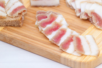 Raw bacon or ukrainian salo on wooden board on white background. Top view, close up.