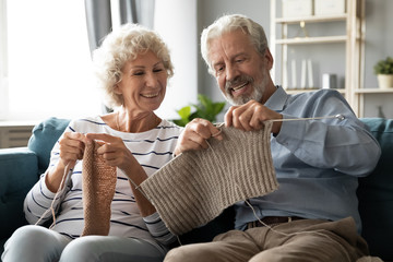 Happy 60s spouses knitting seated on couch enjoy common activity