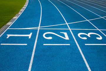 Blue running treadmill track with lane numbers in stadium outdoors.Starting grid of race track at the stadium