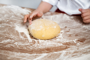 Hands of the child knead dough on a table