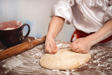 Hands of the child knead dough on a table. Soft focus.
