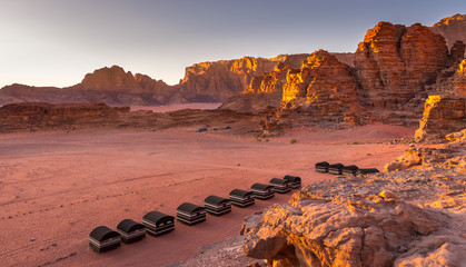 Wadi Rum desert, Jordan. Beautiful aerial view of bedouin camp at sunset from above with tents lined up and red rock formations. Panoramic landscape