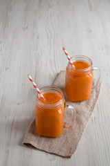 Homemade Mango Carrot Smoothie in glass jars over white wooden background, low angle view. Copy space.