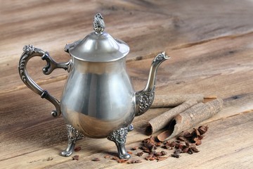 Antique silver teapot, cinnamon and star anise around.  Beautiful luxury silver kettle for tea on the wooden  table.