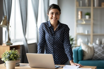 Happy indian girl looking at camera at home with laptop