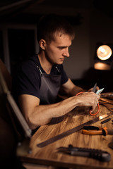 Working process of the leather belt in the leather workshop. Man holding crafting tool and working. Tanner in old tannery. Wooden table background. Close up man arm.