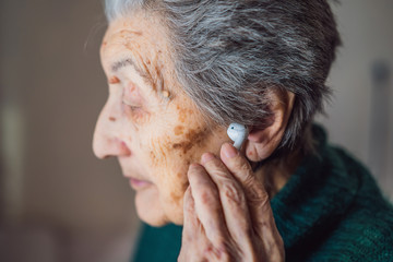 Senior woman listening to music on his smartphone, using modern wireless headphones