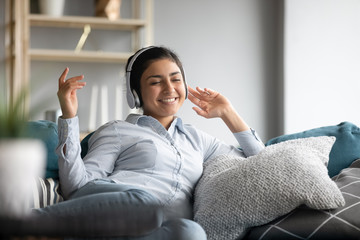 Smiling indian girl wear headphones relax on sofa listening music