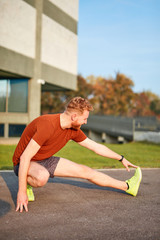 Fototapeta premium Young man exercising / stretching in urban park.