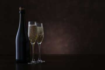 Bottle of champagne and two glasses on brown background