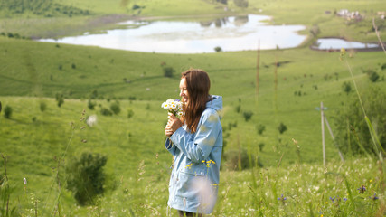 Young happy woman collects field flowers in beautiful nature. Pretty woman walks with flowers in the field