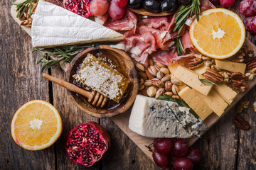 Traditional italian antipasto plate. Assorted cheeses on wooden cutting board. Brie cheese, cheddar slices, gogonzola, walnuts grapes, olives, prosciutto, rosemary and glass of red wine. top view