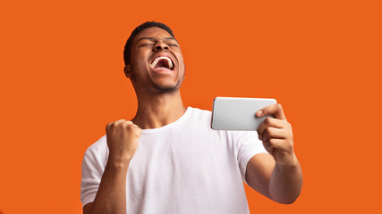 Excited afro guy holding phone celebrating success