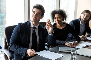 Motivated male employee raise hand participate in team discussion