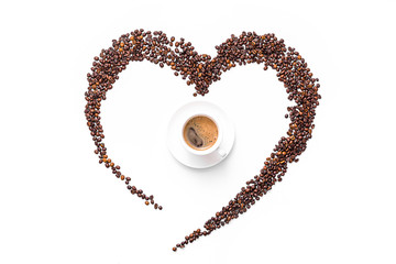 heart made of roasted coffee beans and ground coffee on a white plate and a cup of freshly brewed coffee