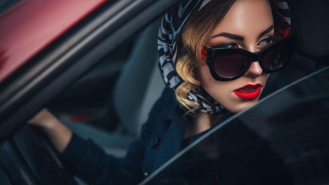 Beautiful brunette sexy spy agent (killer or police) woman in leather jacket and jeans with a gun in her hand driving a car after someone, to catch him