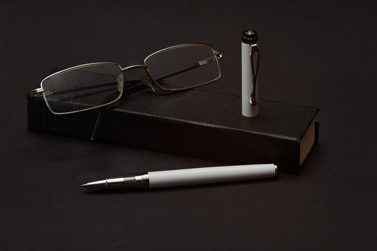 The image of a ballpoint pen and glasses on the box, as a symbol of the development of writing and learning.