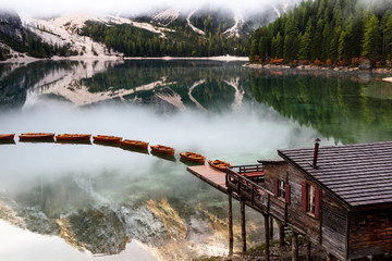 Lago di Braies or Lake Braies in the Dolomites. Lake is surrounded by mountains reflected in the water. Boats are floating on the water surface, on the reflections of the clouds. Italy, South Tyrol. 