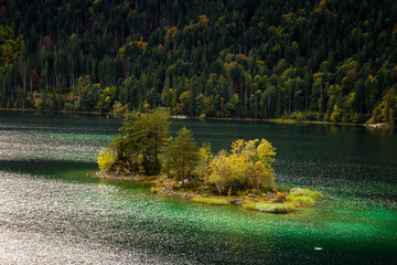 An island with golden trees in the middle of colorful water of Eibsee Lake, situated in the Alps at the foot of Zugspitze mount, Garmisch-Partenkirchen, Bavaria, Germany. 