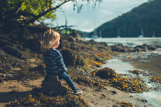 Little toddler sitting on rock by the river in autumn