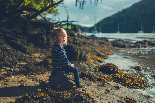 Little toddler sitting on rock by the river in autumn