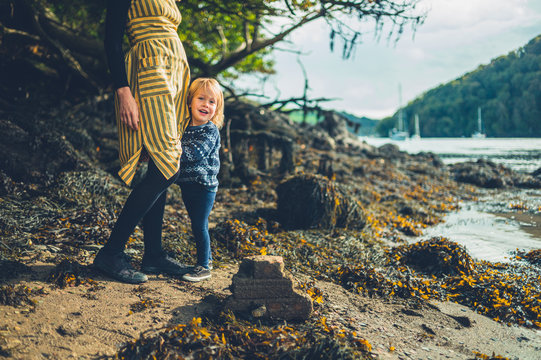 Toddler grabbing his mother's dress by the river in autumn
