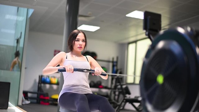 Young woman working out on the rowing machine, training and fitness concept