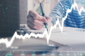 Financial forex graph drawn over hands taking notes background. Concept of research. Double exposure