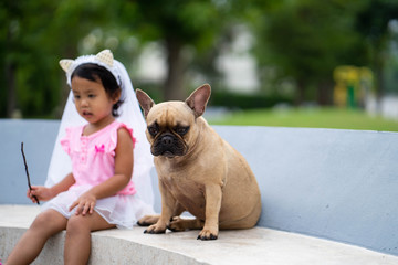 Cute asian girl playing with her lovely french bulldog at marble seat in park.