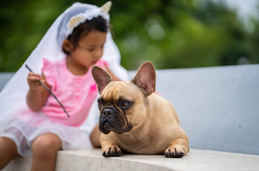 Cute asian girl playing with her lovely french bulldog at marble seat in park.