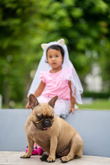 Cute asian girl playing with her lovely french bulldog at marble seat in park.