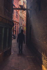Obraz na płótnie Canvas man walking down an narrow alley in a beam of light