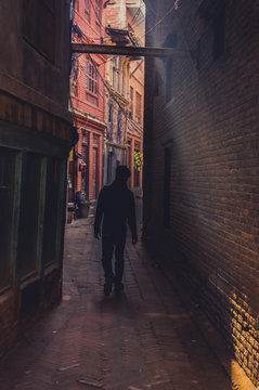 Man Walking Down An Narrow Alley In A Beam Of Light