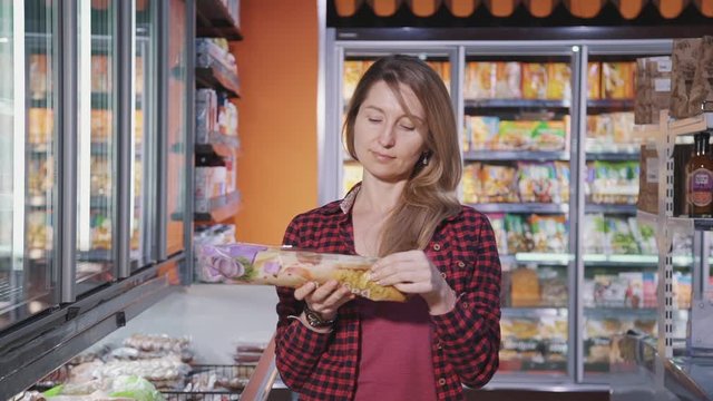 Happy american woman holding baguette in hand while shopping in supermarket. Front view of young smiling female watching content of bakery product standing in grocery shop. Concept: business, customer