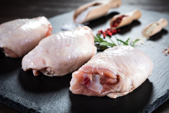 Raw chicken thigs on black stone on wooden background