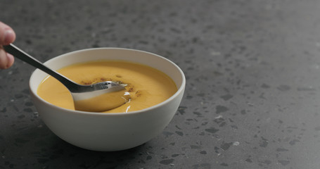 man eating pumpkin cream soup in white bowl on terrazzo countertop