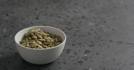 pumpkin seeds in white bowl on terrazzo countertop with copy space
